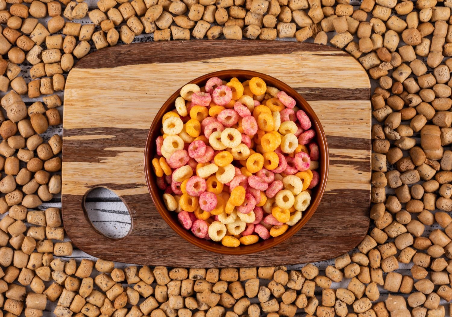 Dog eating from a food bowl with grain-free kibble and whole grains displayed beside it